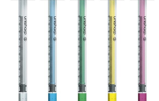 Five Syringes With Colored Liquids (gray, Blue, Green, Yellow, And Pink) Lined Up In A Row On A White Background.